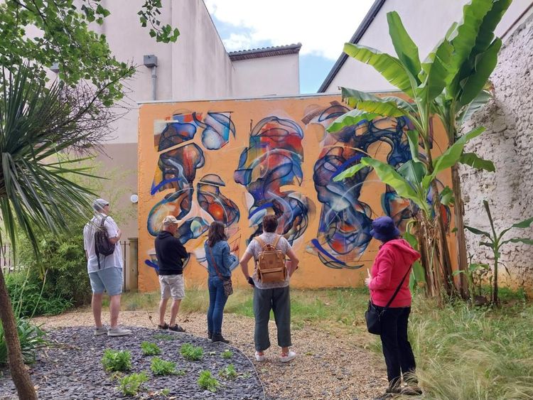 Un groupe de visiteurs devant un mur peint en street art, dans un jardin d'Eauze